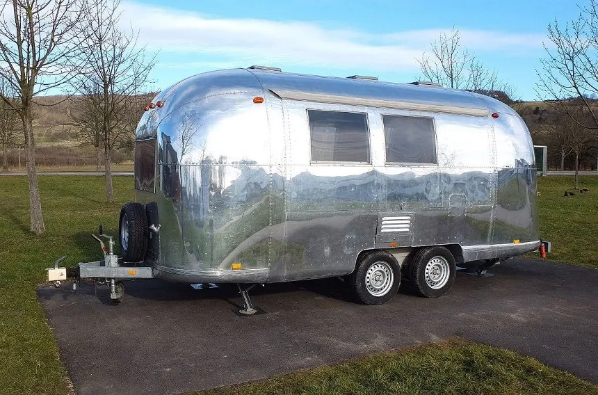 Parked shiny chrome trailer outside with trees and a hill in the background.